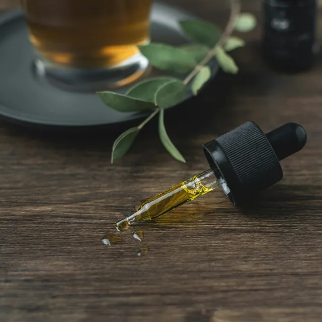 Amber dropper bottle of CBD oil beside dried botanicals